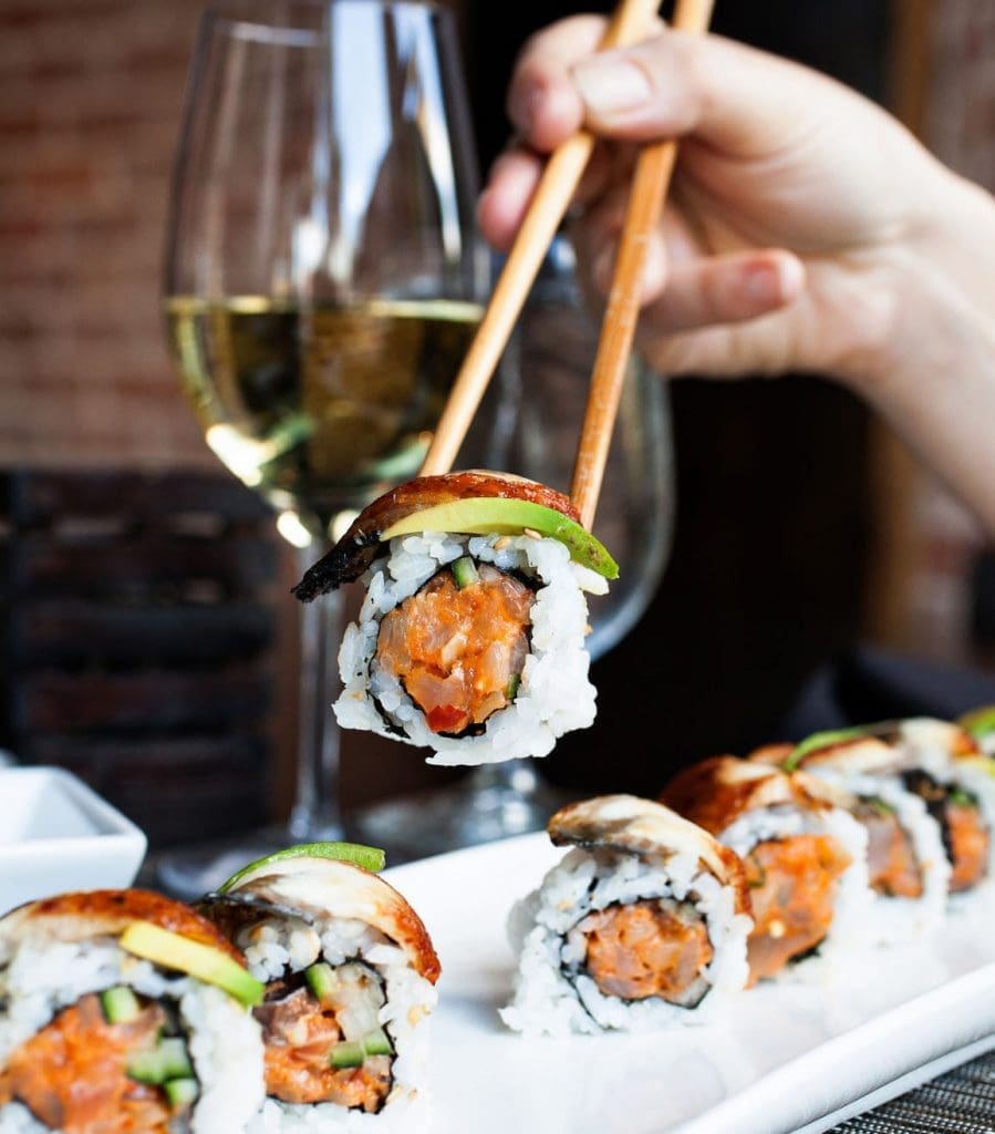 A closeup of a sushi roll being picked up with chopsticks