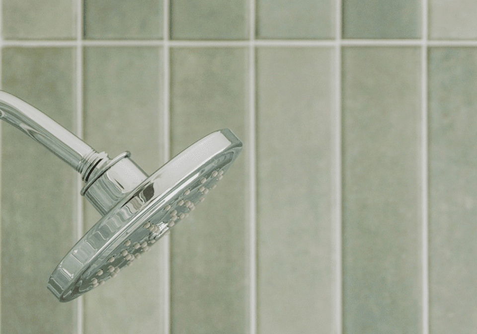 Showerhead against green tiled bathroom wall. Showerhead against green tiled bathroom wall.